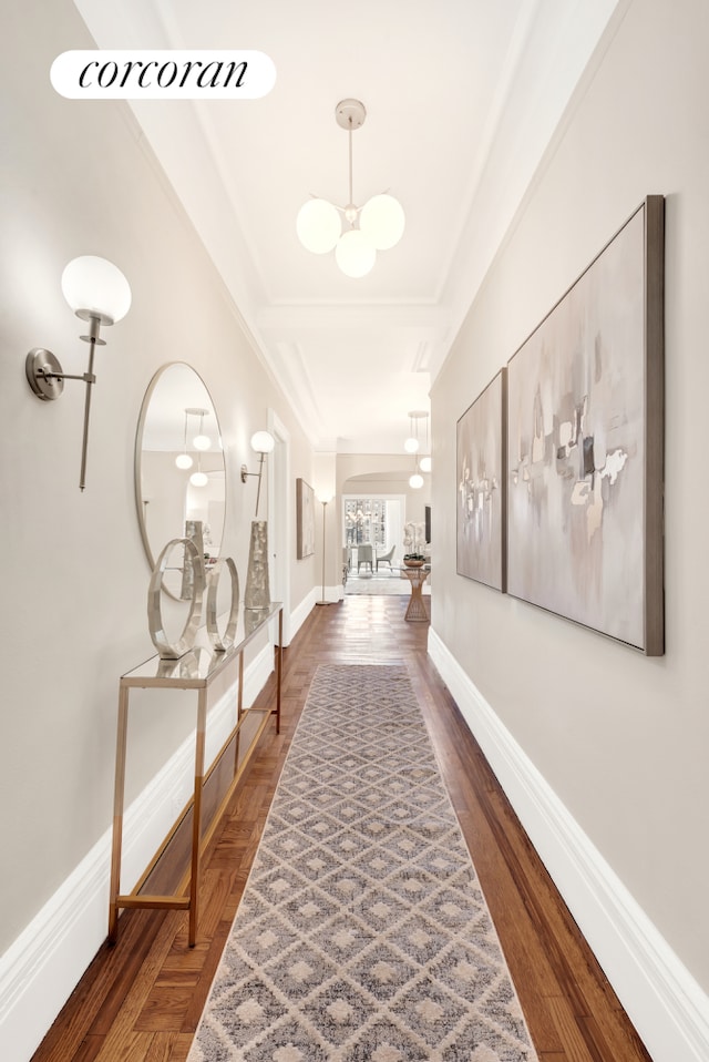 corridor with an inviting chandelier, wood finished floors, and baseboards