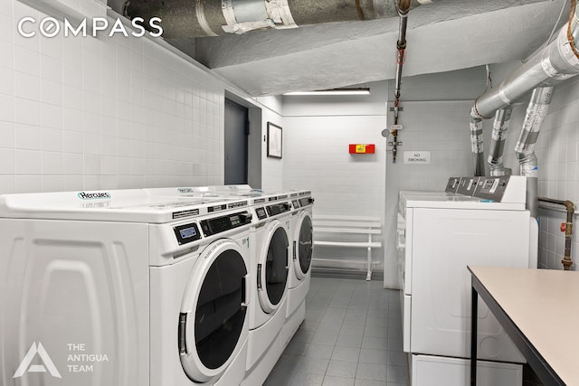 common laundry area with tile patterned flooring, washer and dryer, a textured ceiling, and tile walls