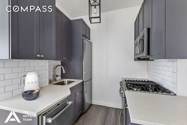 kitchen with a sink, stainless steel appliances, light countertops, baseboards, and dark wood-style flooring