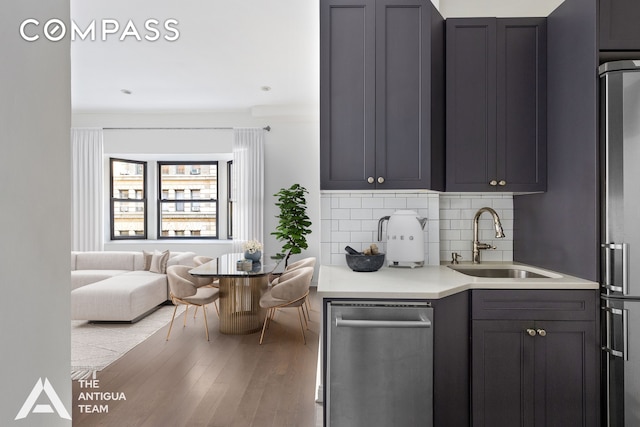 kitchen featuring wood finished floors, refrigerator, a sink, light countertops, and tasteful backsplash