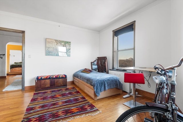 bedroom with baseboards, arched walkways, wood finished floors, and crown molding