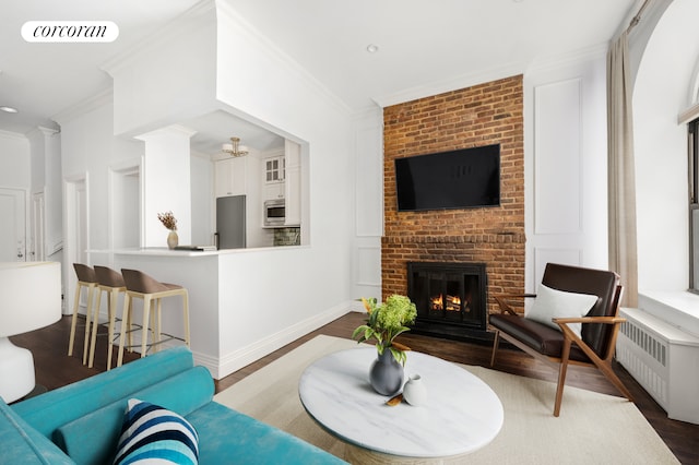 living area with radiator, dark wood-style floors, visible vents, ornamental molding, and a brick fireplace