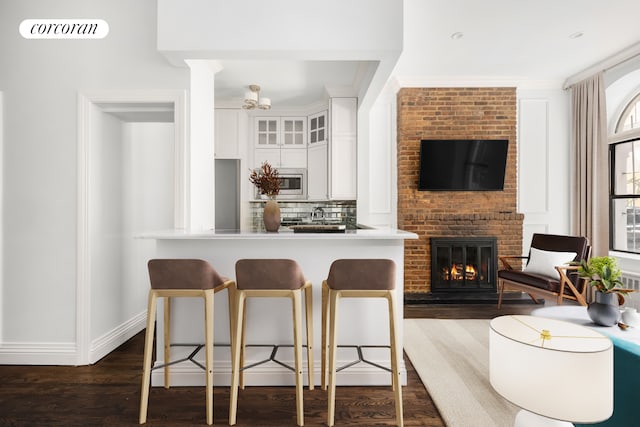 kitchen with visible vents, a kitchen breakfast bar, glass insert cabinets, a brick fireplace, and dark wood-style flooring