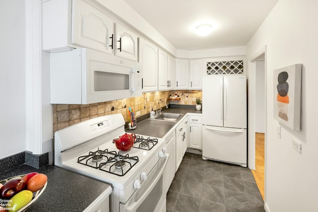 kitchen with a sink, tasteful backsplash, dark countertops, white cabinetry, and white appliances