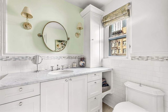 bathroom featuring a wainscoted wall, toilet, tile walls, and vanity