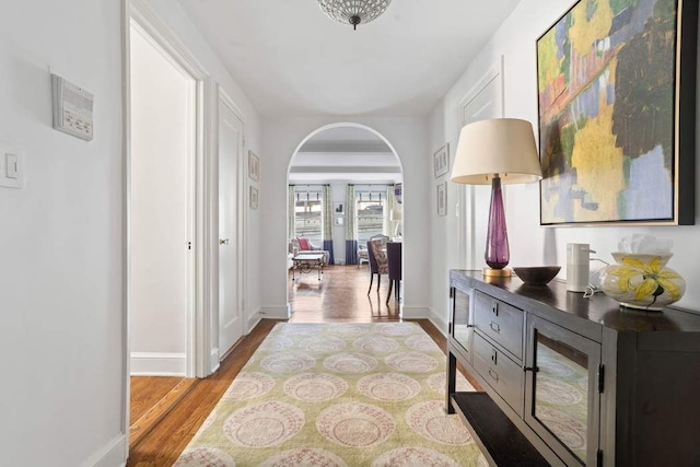 hall featuring wood finished floors, arched walkways, and baseboards