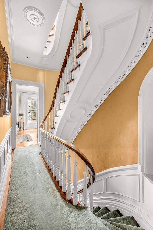 staircase with ornamental molding, wainscoting, and a decorative wall