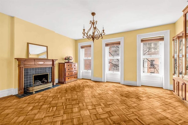 unfurnished living room with a tiled fireplace, a notable chandelier, and baseboards