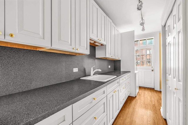 kitchen with a sink, decorative backsplash, white cabinetry, dark countertops, and light wood-type flooring