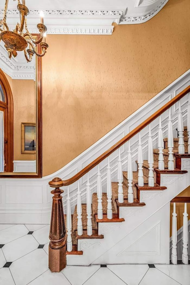 stairs with a chandelier, tile patterned flooring, and wainscoting