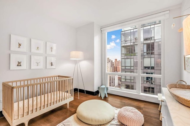 bedroom with a view of city, a nursery area, wood finished floors, and baseboards