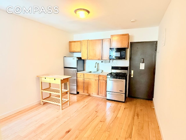 kitchen with a sink, freestanding refrigerator, black microwave, light wood-style floors, and range with gas stovetop