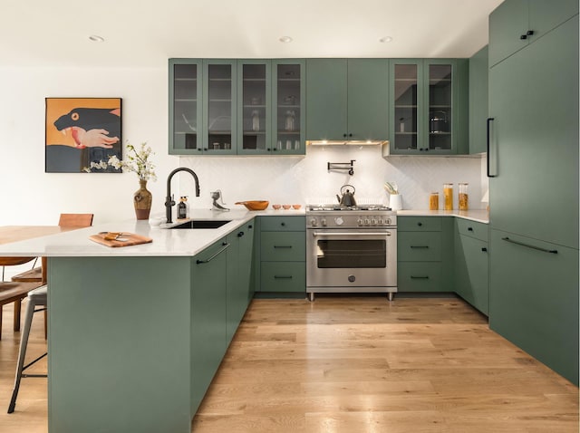 kitchen with light wood finished floors, a breakfast bar area, premium appliances, a peninsula, and a sink