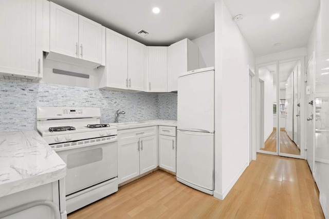 kitchen featuring visible vents, white appliances, light wood-style floors, and a sink