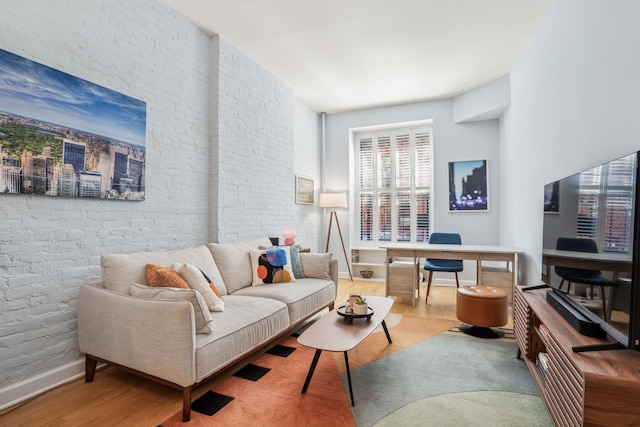 living room with wood finished floors, baseboards, and brick wall