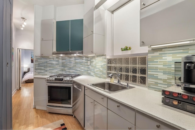 kitchen featuring decorative backsplash, appliances with stainless steel finishes, light wood-type flooring, and a sink