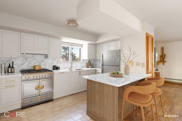 kitchen featuring a sink, double oven range, freestanding refrigerator, a breakfast bar area, and decorative backsplash