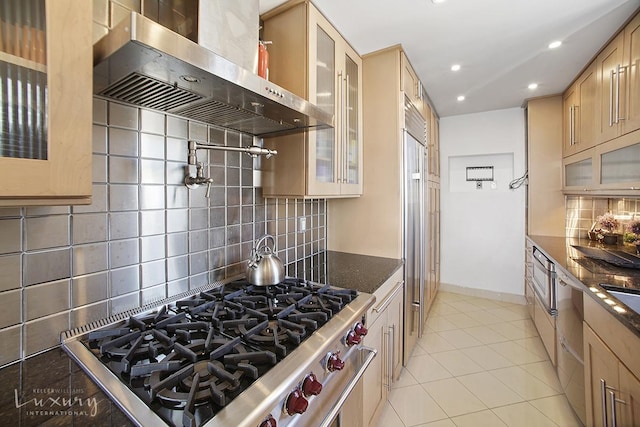 kitchen featuring range hood, dark stone countertops, light tile patterned floors, light brown cabinets, and decorative backsplash