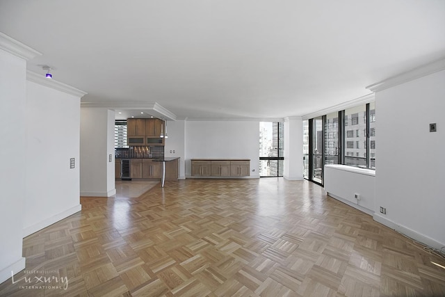 unfurnished living room with wine cooler, baseboards, and ornamental molding