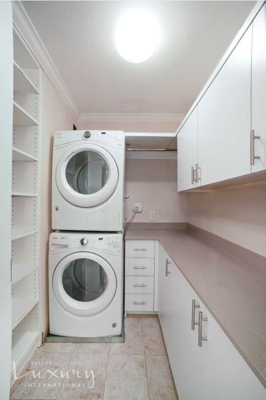 clothes washing area with stacked washer and dryer, light tile patterned floors, cabinet space, and ornamental molding