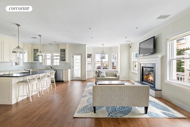 living room with a glass covered fireplace, visible vents, a healthy amount of sunlight, and wood finished floors