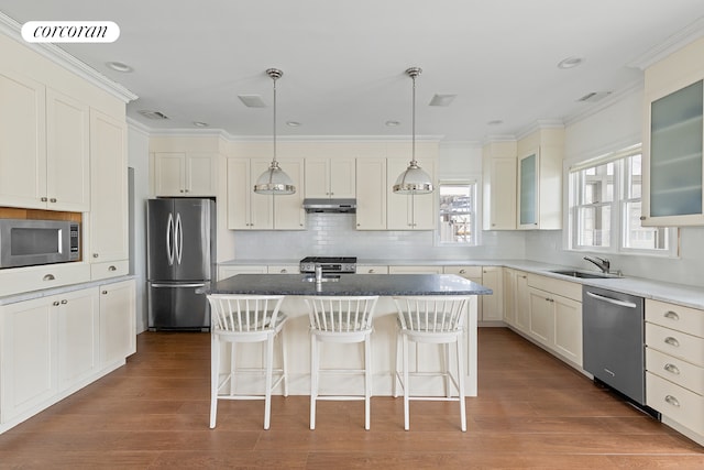 kitchen with visible vents, a sink, stainless steel appliances, under cabinet range hood, and a kitchen bar