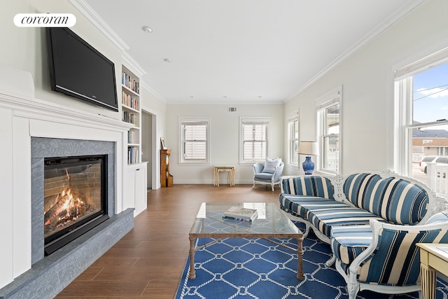 living area featuring visible vents, dark wood-style floors, a glass covered fireplace, crown molding, and baseboards