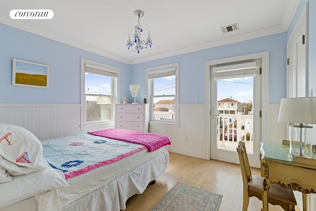 bedroom with visible vents, crown molding, light wood-type flooring, and a wainscoted wall