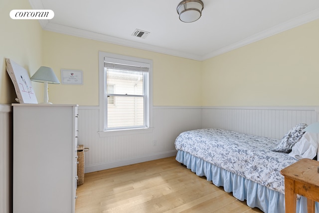 bedroom with crown molding, wood finished floors, a wainscoted wall, and visible vents