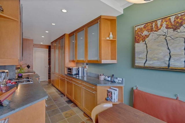 kitchen featuring dark countertops, glass insert cabinets, recessed lighting, stainless steel gas stovetop, and open shelves