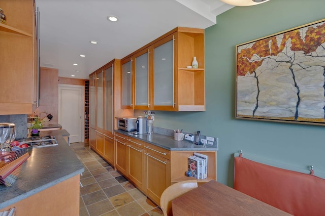 kitchen featuring stainless steel gas cooktop, open shelves, recessed lighting, glass insert cabinets, and dark countertops