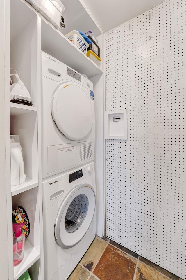 laundry room featuring laundry area, stacked washer / dryer, and stone tile floors