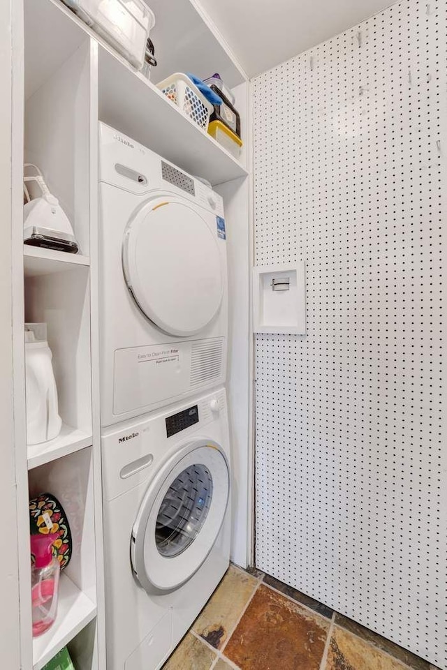 washroom with laundry area, stacked washer / dryer, and stone finish floor