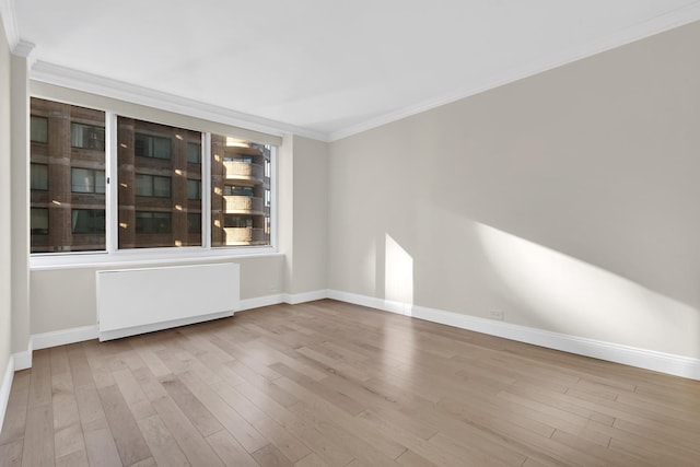 spare room featuring crown molding, radiator, wood finished floors, and baseboards