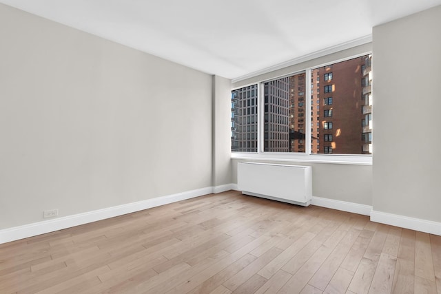 empty room with baseboards, wood finished floors, and radiator heating unit