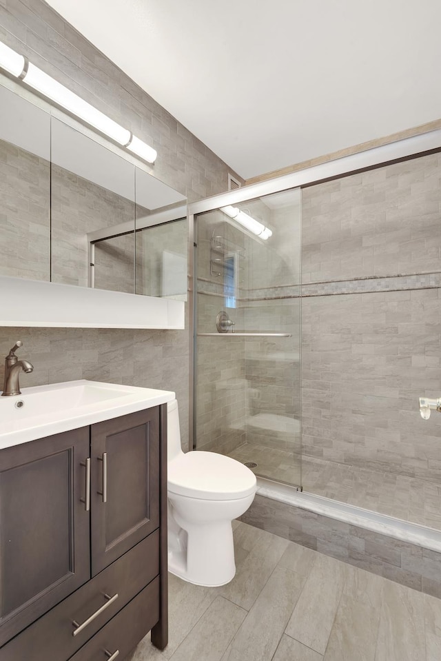 bathroom featuring toilet, tile walls, a shower stall, decorative backsplash, and vanity