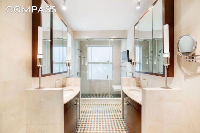 bathroom featuring a stall shower, tile walls, two vanities, and a sink