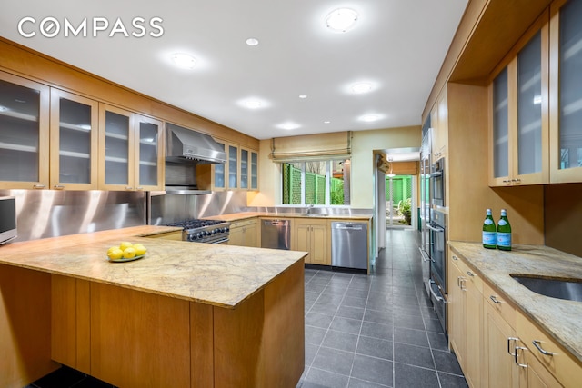 kitchen featuring a sink, appliances with stainless steel finishes, a peninsula, and wall chimney exhaust hood