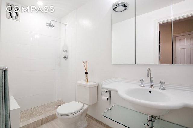 bathroom featuring toilet, visible vents, a tile shower, and a sink