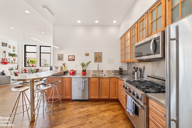 kitchen featuring stainless steel countertops, light wood-type flooring, a peninsula, stainless steel appliances, and a sink