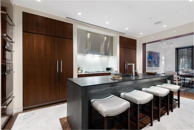 bar featuring stovetop, wall chimney range hood, recessed lighting, and a sink