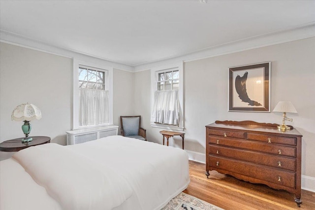 bedroom with crown molding, radiator, light wood-type flooring, and baseboards