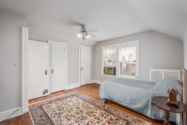 bedroom featuring wood finished floors, baseboards, ceiling fan, vaulted ceiling, and multiple closets