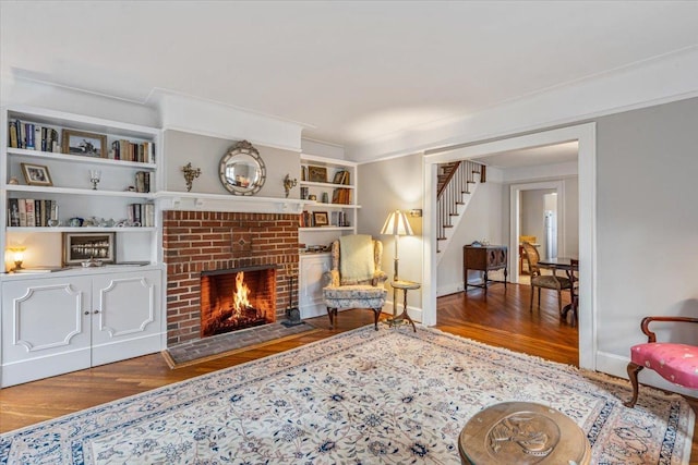 living area featuring a brick fireplace, stairway, built in shelves, and wood finished floors