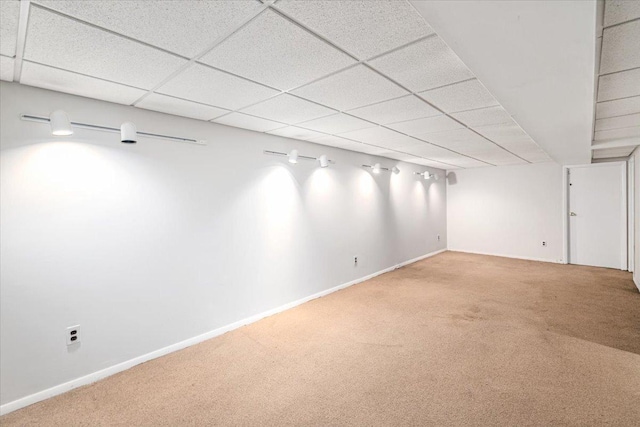 basement with carpet flooring, a paneled ceiling, and baseboards