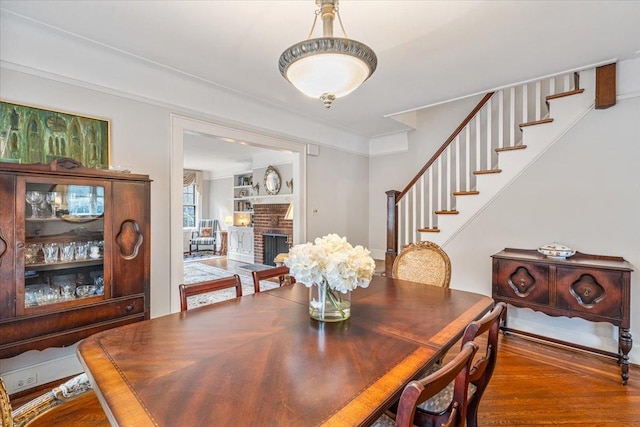 dining space featuring stairway, wood finished floors, a brick fireplace, and ornamental molding