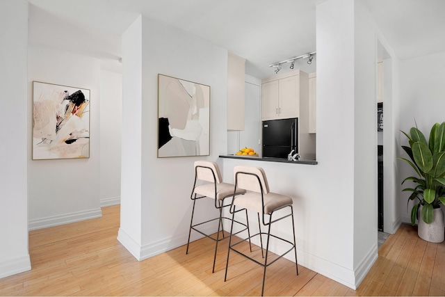 kitchen featuring a kitchen bar, light wood-style flooring, and black refrigerator