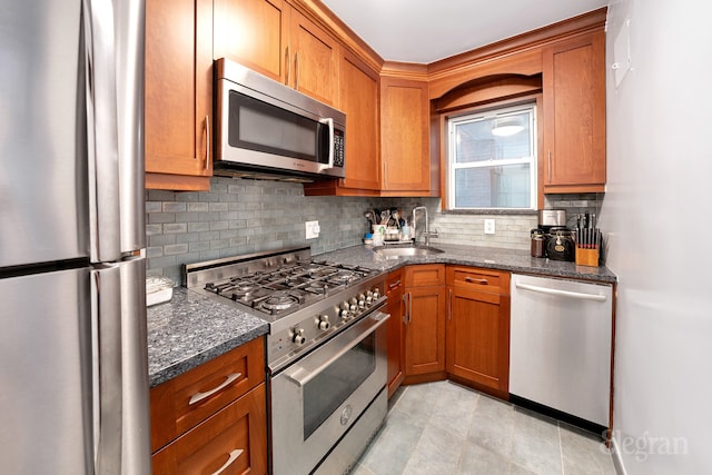 kitchen featuring tasteful backsplash, dark stone counters, brown cabinets, appliances with stainless steel finishes, and a sink