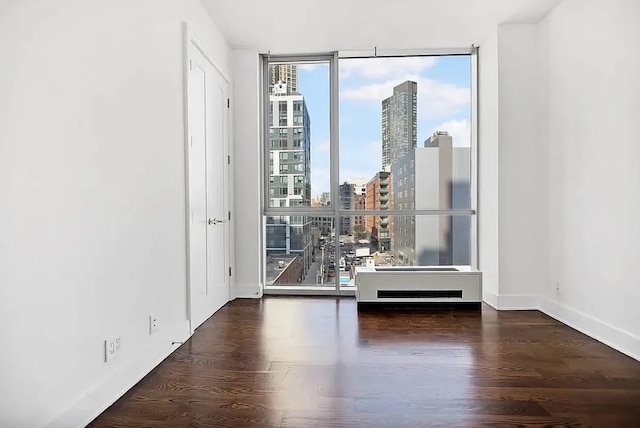 empty room with a view of city, wood finished floors, baseboards, and expansive windows