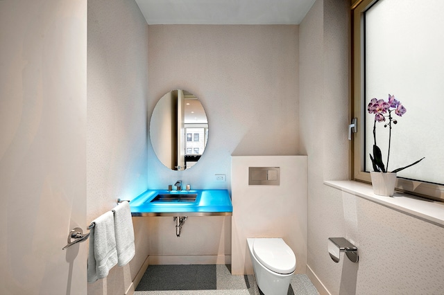 half bath featuring toilet, baseboards, and a sink